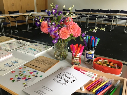 Lettering-Bücher, Brushpen, Lettering-Guide und Blumen auf einem Tisch in einem Workshop-Raum. Foto: Janne Klöpper
